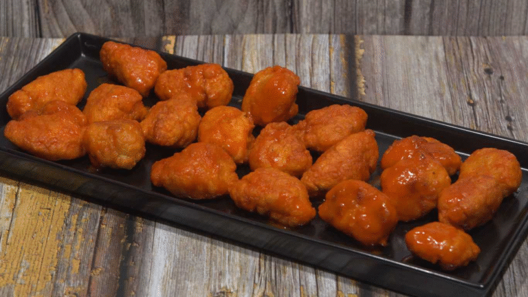 Chicken bone in wings on a black serving tray, coated in a red sauce.