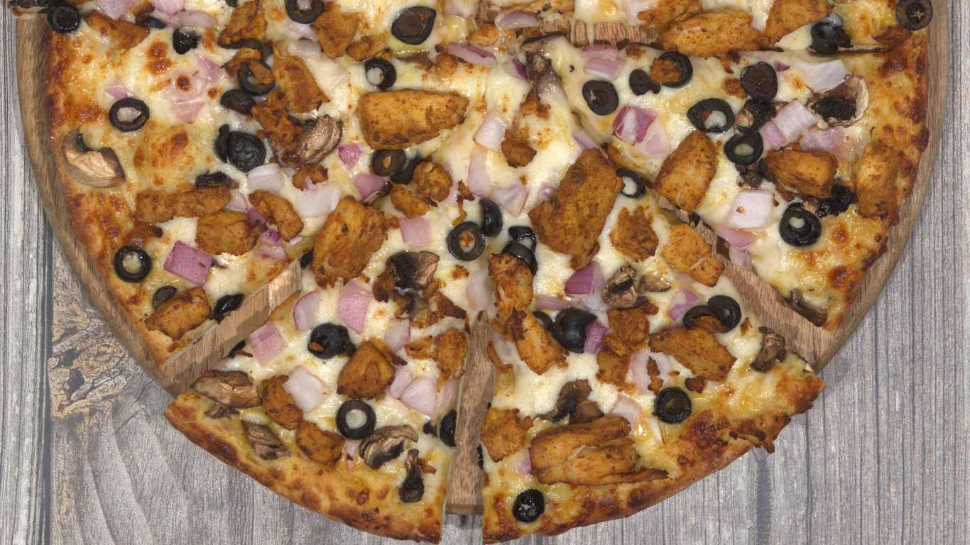 Curry chicken pizza with black olives, red onions, and mushrooms on a wooden board.