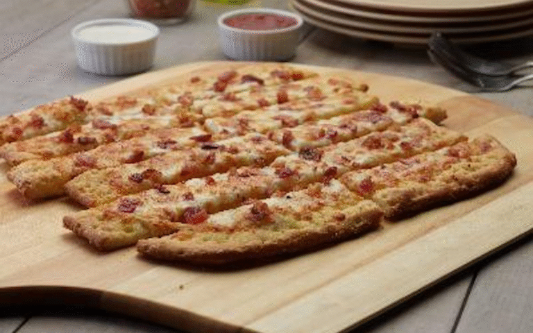 Cheesy garlic bread sticks with bacon on a wooden board.