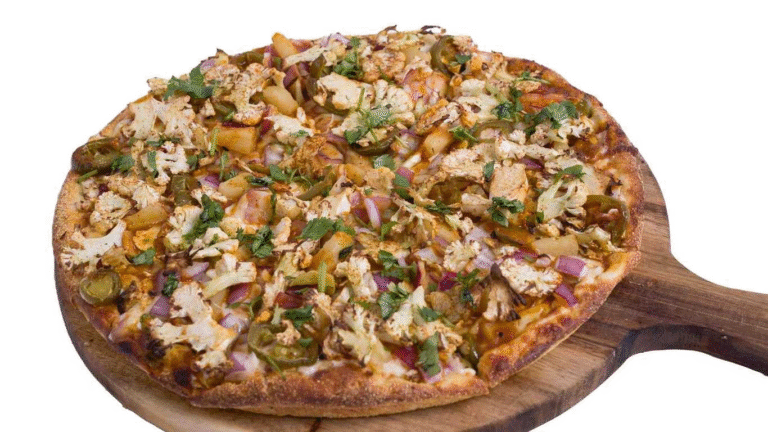 Achari Gobi Pizza on a wooden board, topped with cauliflower, red onion, and jalapeños.