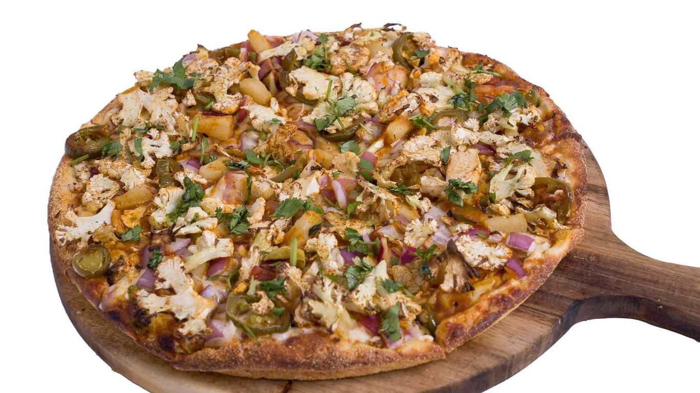 Achari Gobi Pizza on a wooden board, topped with cauliflower, red onion, and jalapeños.