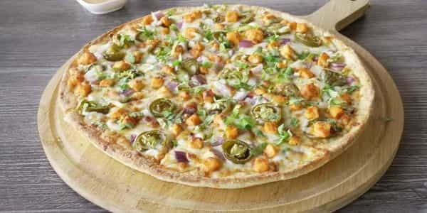 Achari Paneer Pizza: Close-up of a pizza topped with paneer, jalapeños, onions, and herbs on a wooden board.
