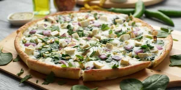 Pesto chicken pizza with spinach and red onion on a wooden board, surrounded by fresh spinach leaves.
