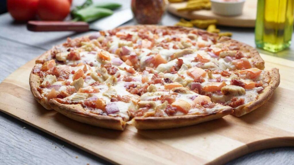 BBQ chicken pizza on a wooden board, sliced and ready to eat.