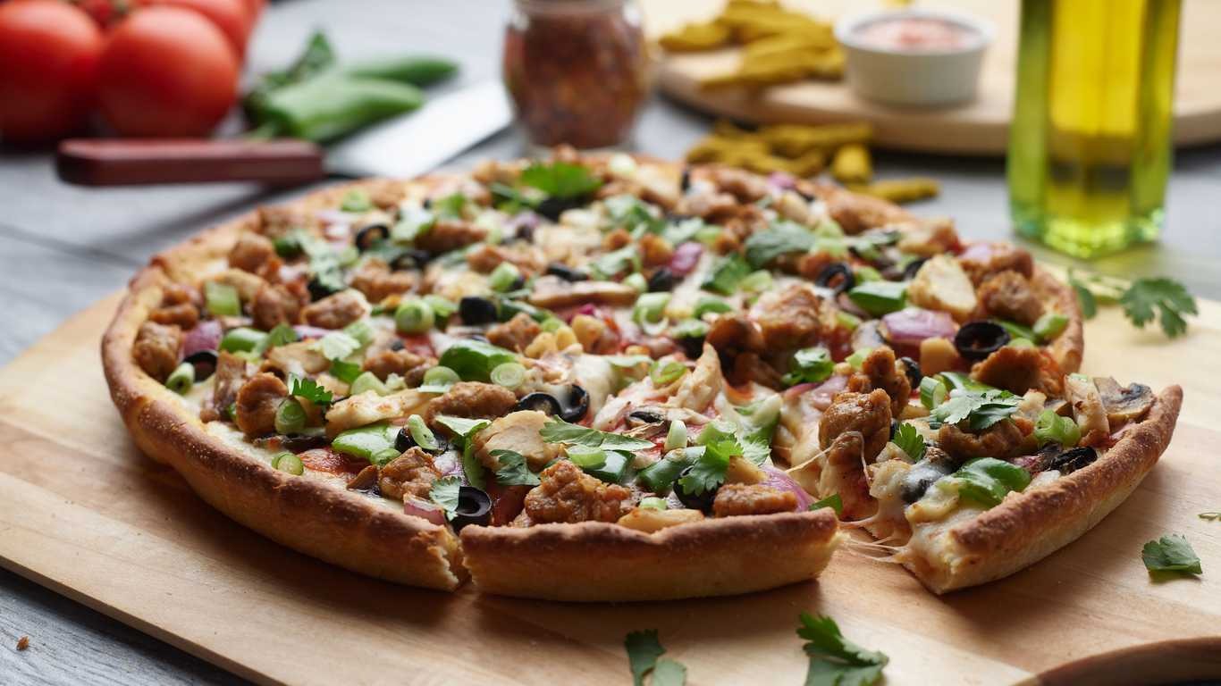 Loaded pizza with chicken, olives, mushrooms, onions, and green peppers on a wooden board.