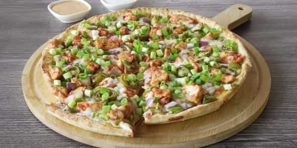 Manchurian Chicken Pizza cut on a wooden board, topped with green onions and jalapenos.