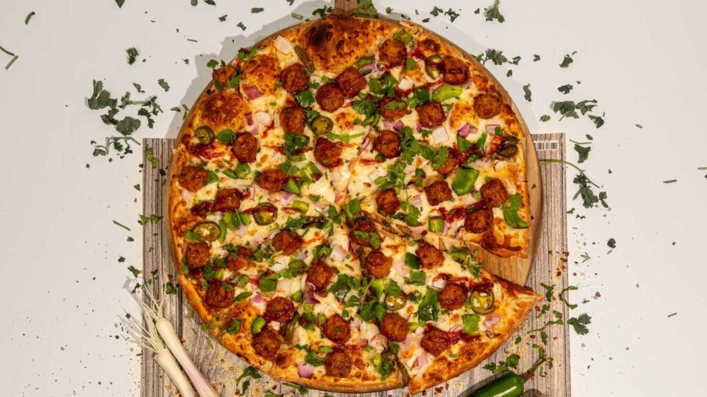 Manchurian Paneer Pizza with paneer balls, jalapeños, red onion, and cilantro on a wooden board.