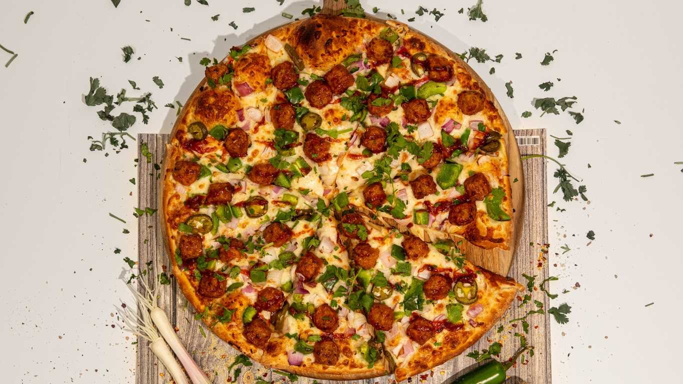 Manchurian Paneer Pizza with paneer balls, jalapeños, red onion, and cilantro on a wooden board.