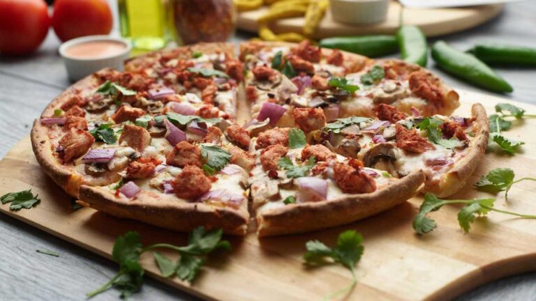 Tandoori chicken pizza with red onions, mushrooms, and cilantro on a wooden board.