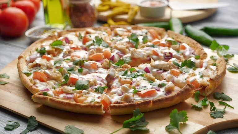 Bombay Garlic Chicken Pizza, sliced on a wooden board, topped with fresh cilantro and red onion.