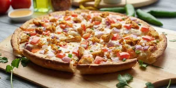 Butter chicken pizza on a wooden board, topped with chicken, tomatoes, and red onions.