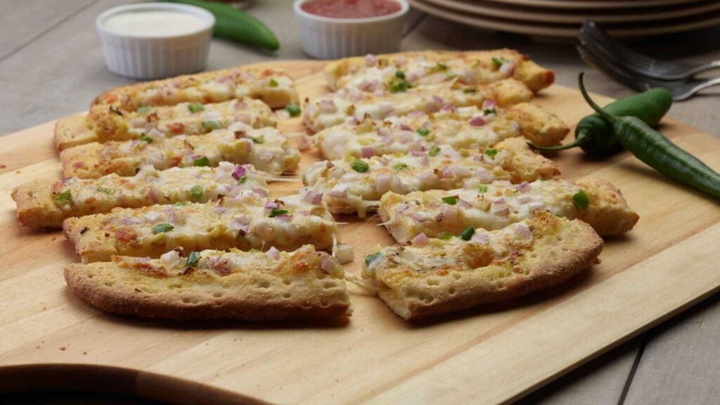 Curry Masala Bread: Close-up of sliced, cheesy bread topped with red onion and green chilies on a wooden board.