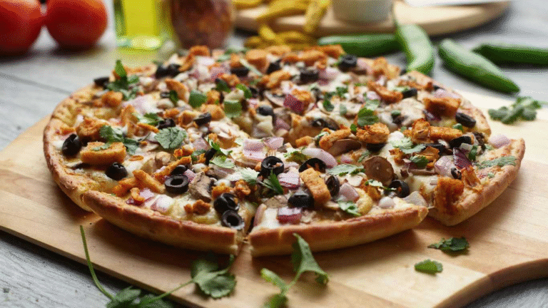 Curry Paneer Pizza on a wooden board, topped with paneer, olives, onions, and cilantro.