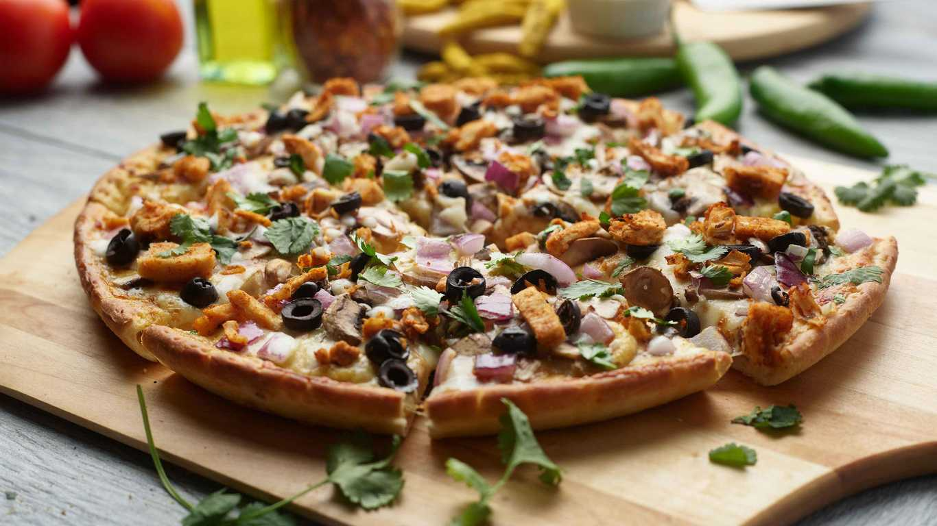 Curry Paneer Pizza on a wooden board, topped with paneer, olives, onions, and cilantro.