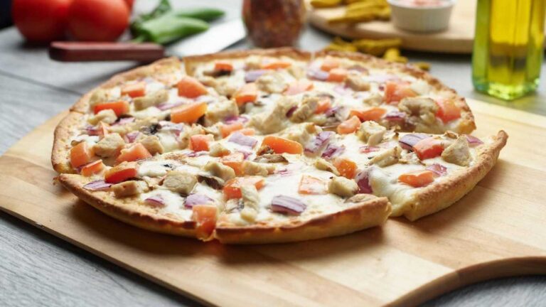 Creamy garlic chicken pizza with tomatoes and red onion on a wooden board, cut into slices.
