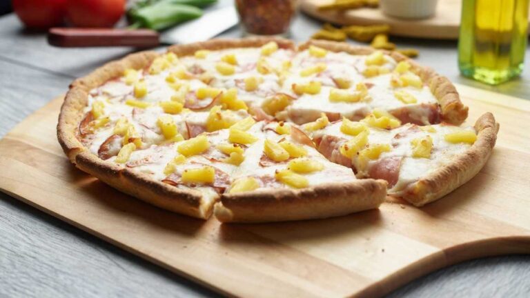 Delicious Hawaiian pizza with pineapple and ham on a wooden board.