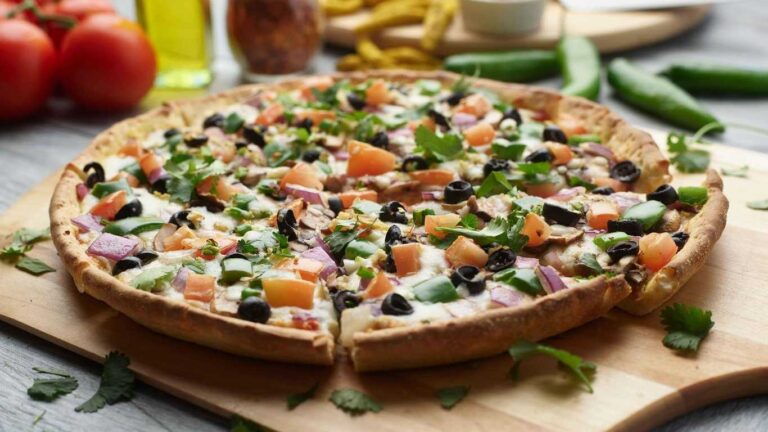 Indian veggie pizza with tomatoes, olives, red onions, and cilantro on a wooden board.