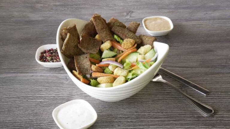 Tandoori Lamb salad with lettuce, cucumbers, carrots, croutons, and dressing served in a white bowl.
