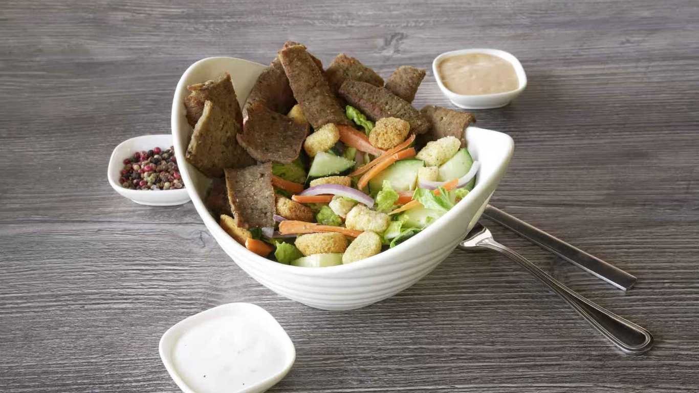 Tandoori Lamb salad with lettuce, cucumbers, carrots, croutons, and dressing served in a white bowl.