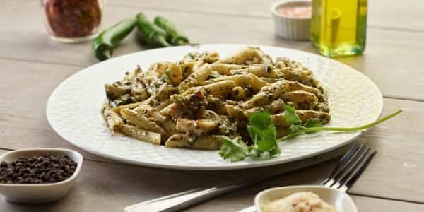 Palak Paneer Pasta on a white plate, garnished with cilantro and green chilies.