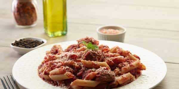 Penne meatball pasta on a white plate, garnished with basil.
