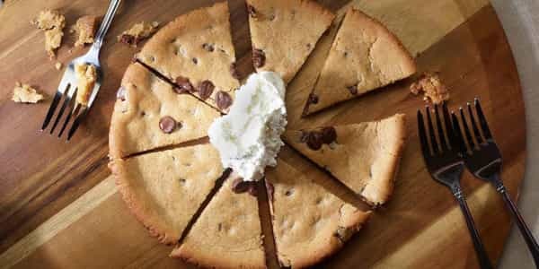Pizza cookie cut into slices with whipped cream on a wooden board.