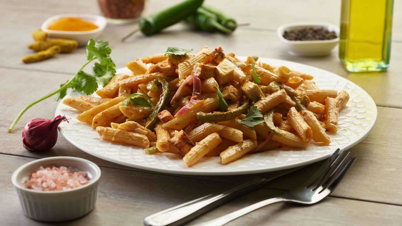 Shahi Paneer Pasta: Penne pasta with paneer cheese and vegetables on a white plate.