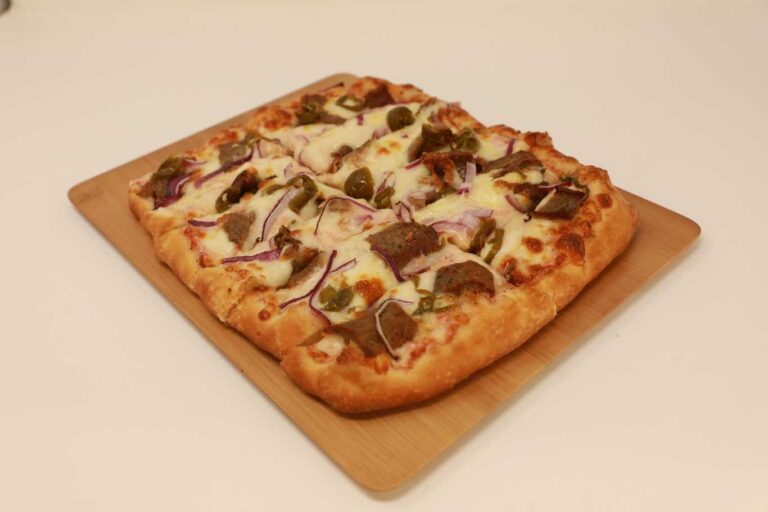 Spicy lamb flatbread pizza with red onions and jalapeños on a wooden board.