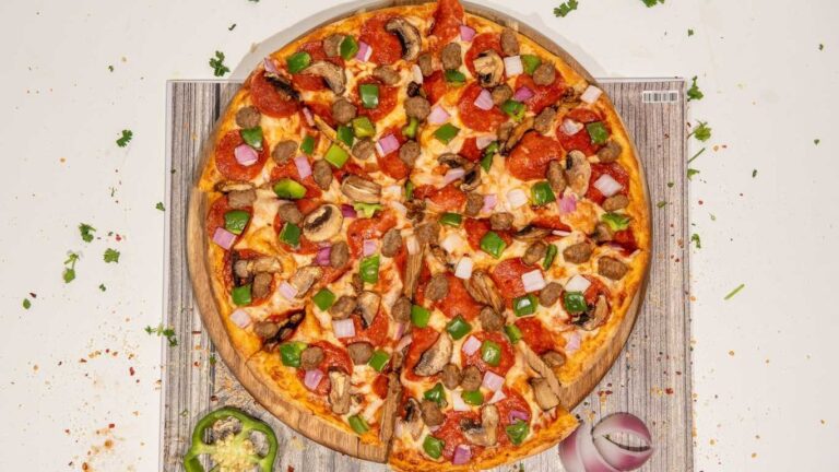 Supreme pizza with pepperoni, sausage, mushrooms, green peppers, and red onions on a wooden board.