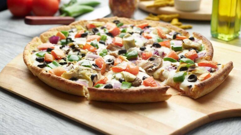 Vegenation Pizza with artichokes, tomatoes, olives, mushrooms, peppers, and red onion on a wooden board.