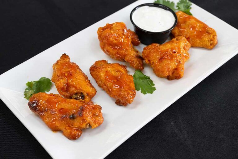 Halal chicken wings with sauce, served on a white plate with dipping sauce.