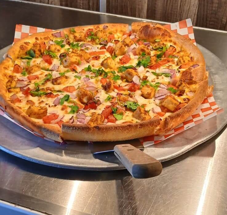 Chicken pizza with red onions and tomatoes on a metal tray, ready for an unlimited pizza buffet.