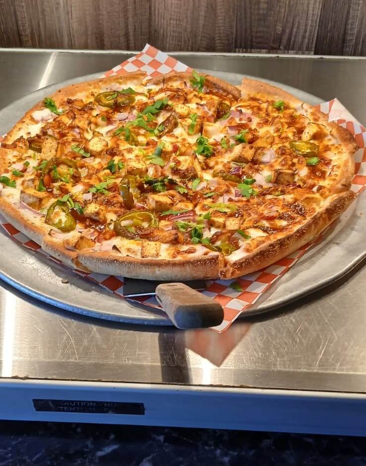 Pizza with chicken, jalapeños, and red onion on a checkered liner, ready for an unlimited pizza buffet.