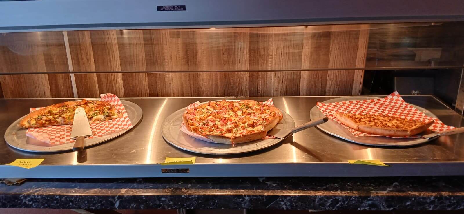 Pizza buffet with various pizzas under a warming display.