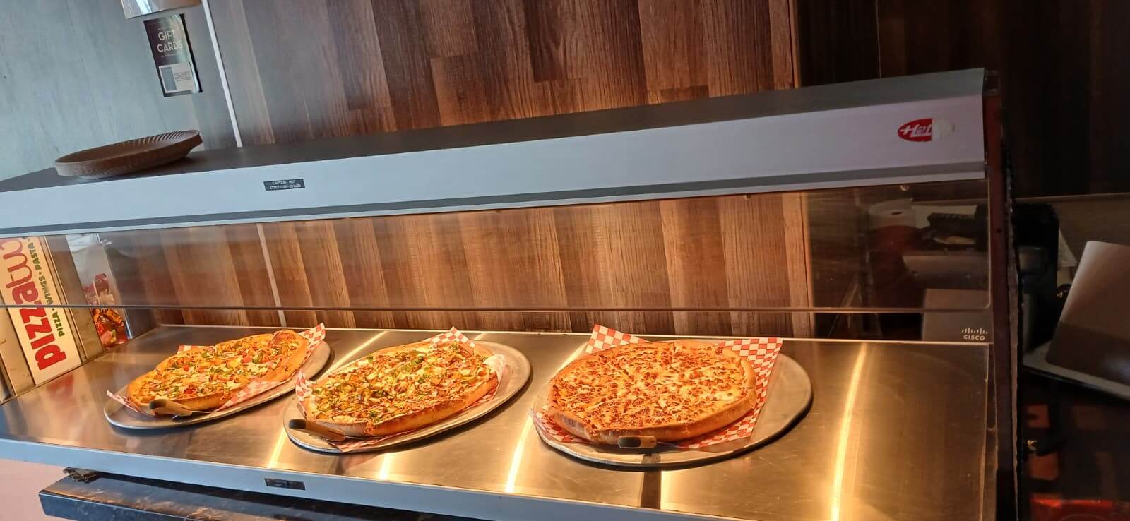 Pizza buffet display case with three pizzas. Unlimited Pizza Buffet.