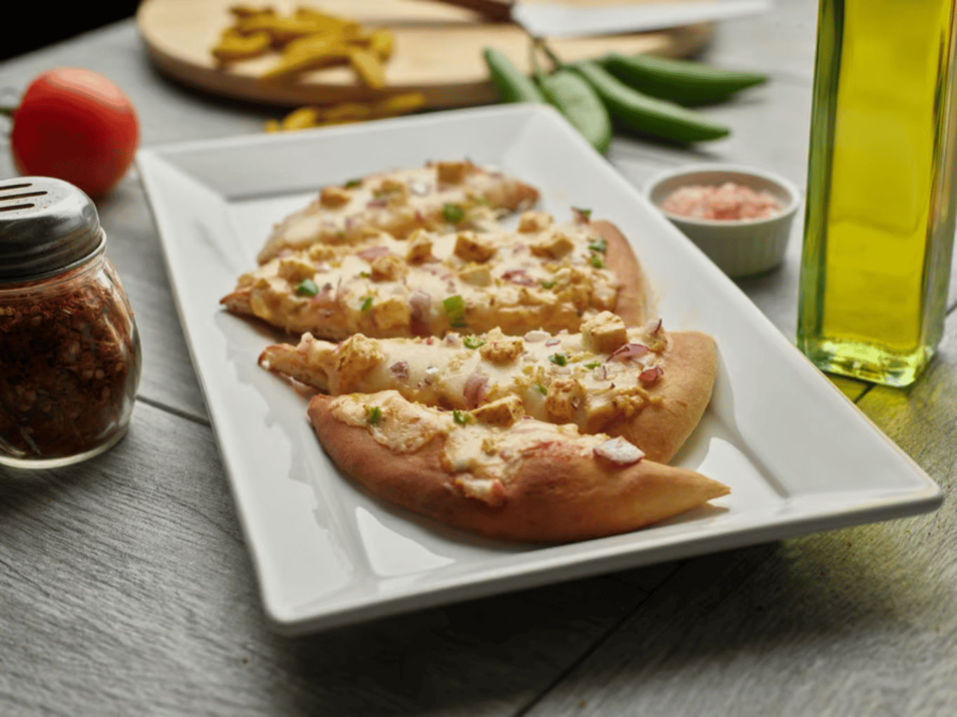 Shahi paneer naan pizza slices on a white platter with ingredients.